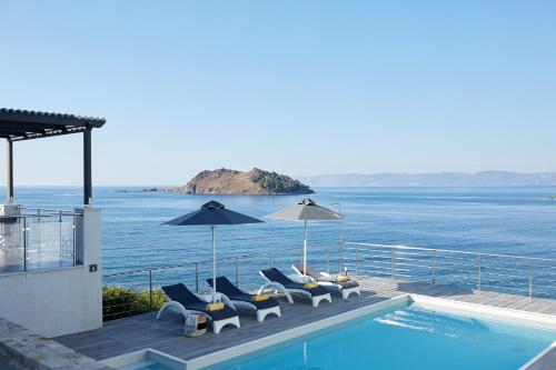 a pool with chairs and umbrellas next to the water at Eleia Seafront Rooms & Villas in Petra