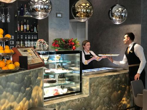 a woman giving a man a plate of food at a counter at Hotel Colosseo Tirana in Tirana