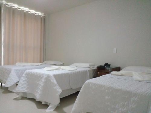 a room with three beds with white sheets at Brito Hotel in Resplendor