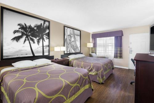 a hotel room with two beds and a palm tree on the wall at Super 8 by Wyndham Ellenton Bradenton Area in Ellenton