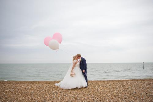 a bride and groom standing on the beach with balloons at Hythe Imperial Hotel, Spa & Golf in Hythe