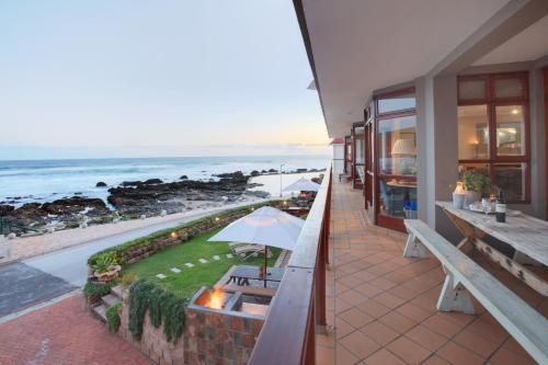 a patio with a table and an umbrella and the ocean at Oppiesee Selfcatering Apartments in Herolds Bay