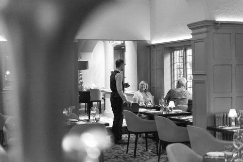a man standing in a restaurant with people sitting at tables at The Crown Manor House Hotel in Lyndhurst