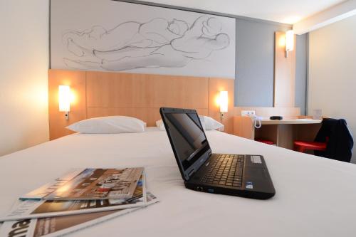 a laptop computer sitting on top of a bed with a magazine at ibis Lyon Part Dieu Les Halles in Lyon