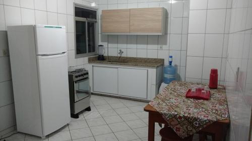 a white kitchen with a table and a refrigerator at Apto Paulino Frente Mar in Piúma