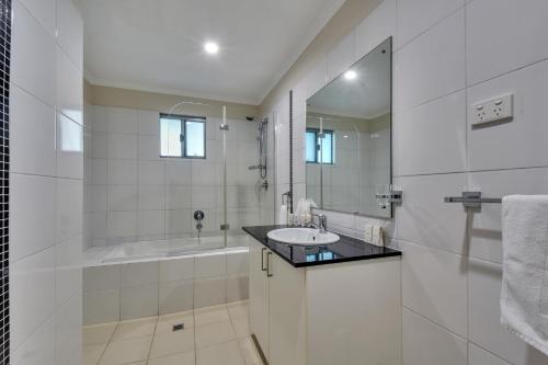 a white bathroom with a sink and a tub at Argus Apartments Darwin in Darwin