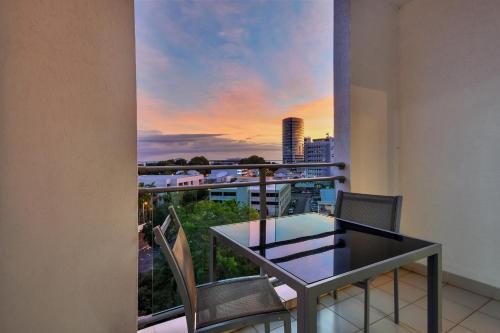 a glass table and chairs on a balcony with a sunset at Argus Apartments Darwin in Darwin