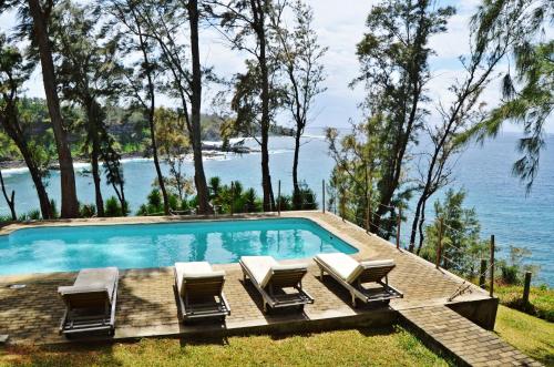a swimming pool with lounge chairs and the ocean at Andrea Lodges in Souillac