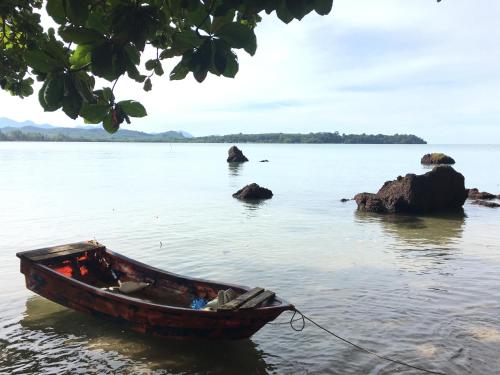 a boat sitting in the water next to some rocks at Sleep Soundly By The Sea in Trat
