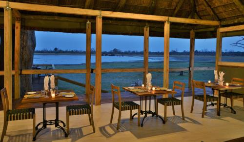 a dining room with tables and chairs and a view of the ocean at Nogatsaa Pans Chobe Lodge in Kasane