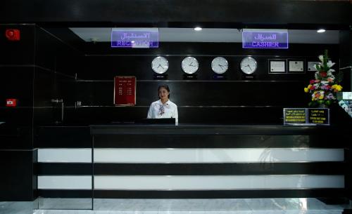 a woman standing behind a counter in a room with clocks at Crystal Palace Hotel in Manama