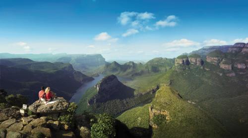two people sitting on the edge of a mountain overlooking a canyon at Blyde Canyon, A Forever Resort in Matibidi