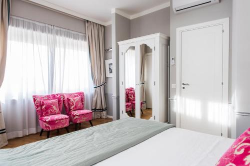 a bedroom with a bed and two pink chairs at La Malandrina - Apartments & Suites in Taormina