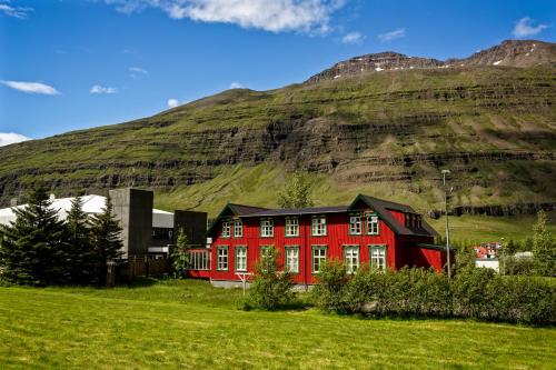 una casa roja frente a una montaña en Hafaldan HI hostel, old hospital building, en Seyðisfjörður