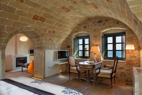 Moni Emvasis Luxury Suites في مونيمفاسيا: غرفة بجدار حجري وطاولة وكراسي