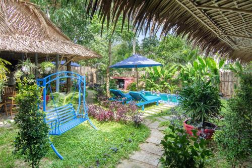 a garden with blue benches and an umbrella at An Bang beach Happy Village in Hoi An