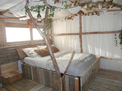 ein Schlafzimmer mit einem Himmelbett mit einem Baum in der Unterkunft le Crusoé à l'étang d'Anty - appartement in Saint-Nabord