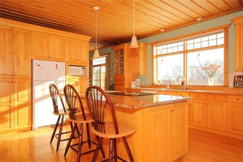 una cocina con armarios de madera y una isla con taburetes. en Rock Hill Bed & Breakfast en Sharbot Lake