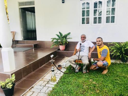 two men sitting on the grass in front of a house at White Villa Airport Transit Hotel in Katunayake
