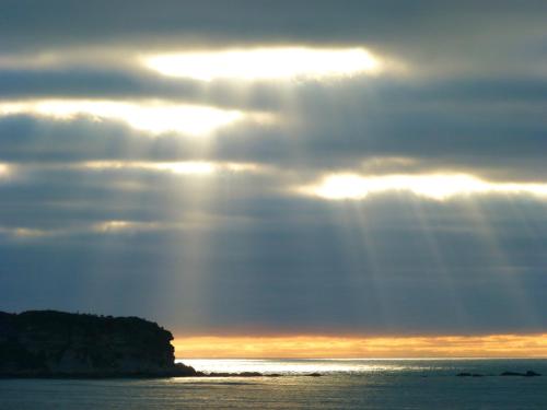 a sun shining through the clouds over the ocean at BeachView Motel in Greymouth