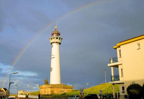 a rainbow behind a lighthouse with a building at Egmond aan Zee Vakantiehuisje in Egmond aan Zee
