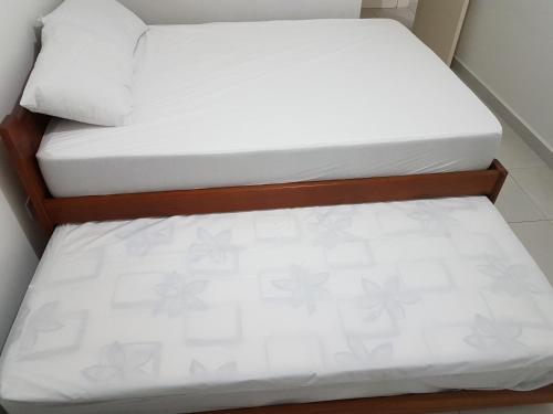 two beds in a small room with white sheets at Apartamento Avenida Wilson in Ubatuba