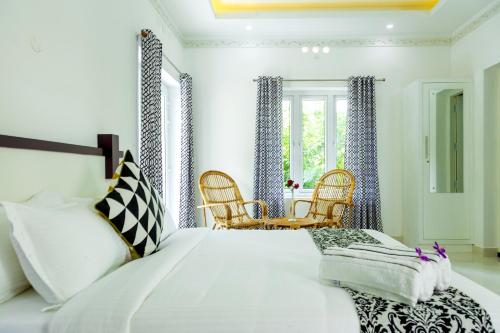 a bedroom with a large white bed and chairs at Bamboo Creak in Thekkady