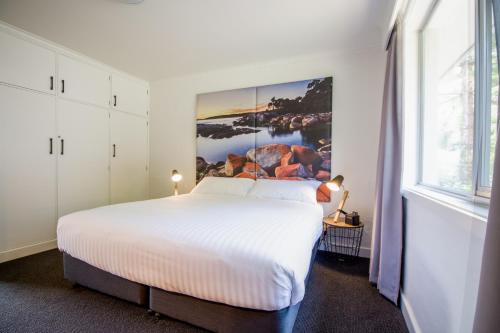 a bedroom with a white bed with a painting on the wall at CBD Apartments Launceston in Launceston
