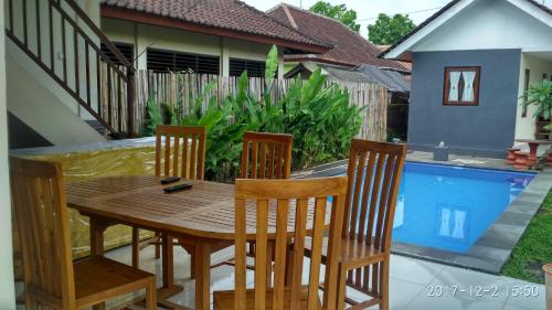 een houten tafel en stoelen op een patio met een zwembad bij Obama House Ubud in Ubud