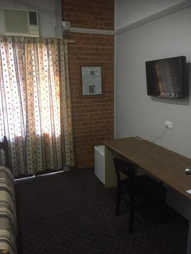 a room with a desk and a table and a television at Heritage Hotel Rockhampton in Rockhampton