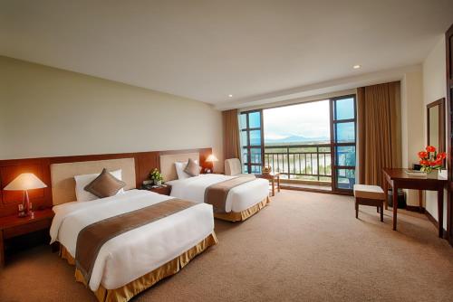 two beds in a hotel room with a large window at Muong Thanh Holiday Hoi An Hotel in Hoi An
