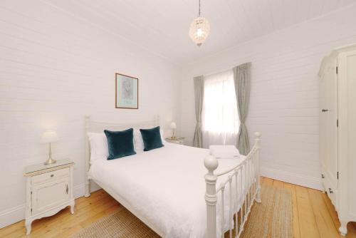 a white bedroom with a white bed with blue pillows at Poets Cottage c1912 Scenic Hikes, Fire, Spa Bath in Wentworth Falls