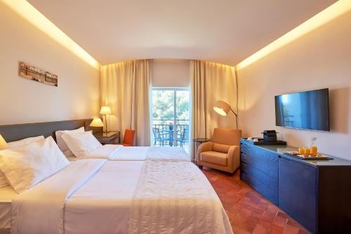 Cette chambre comprend un grand lit et une télévision. dans l'établissement Penina Hotel & Golf Resort, à Portimão