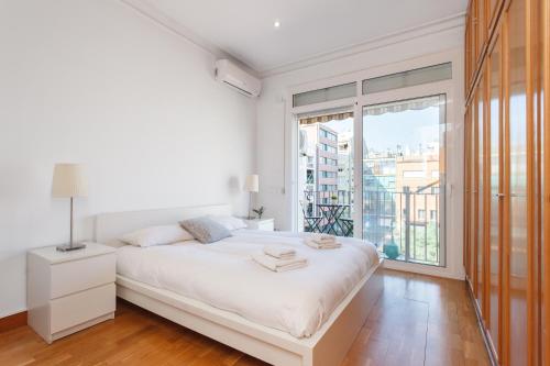 a white bedroom with a bed and a large window at Flateli Aribau in Barcelona