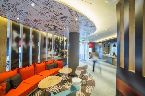 an office lobby with orange couch and tables and a person at Ibis Barcelona Castelldefels in Castelldefels