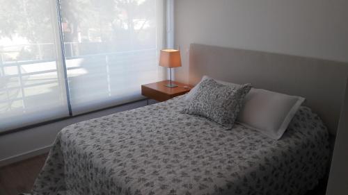 a bedroom with a bed with a lamp and a window at Apartamento Alexander Boulevard in Punta del Este