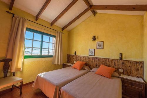 Casa Abuela María في Isora: سريرين في غرفة بجدران صفراء ونافذة