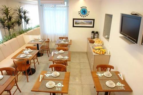 リオデジャネイロにあるHotel Venezuelaのテーブルと椅子、薄型テレビ付きのレストランを提供しています。