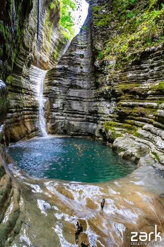a small pool of water in front of a waterfall at En Chora Vezitsa in Vitsa