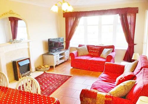 a living room with red couches and a tv at The Beach House! Just Steps from the Beach & Attractions - Perfect for Couples & Family Stays with Private Parking, Large Garden & Fast Free WiFi - The Perfect Seaside Getaway! in Sutton on Sea