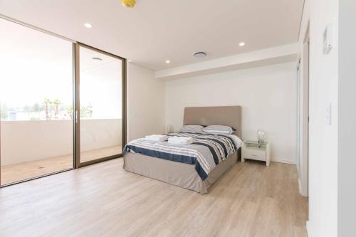 a white bedroom with a bed and a large window at Bluewater Apartments in Kiama