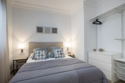 a white bedroom with a large bed with blue pillows at Flatsforyou Cabanyal Beach in Valencia