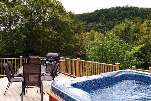 a hot tub on a deck with chairs and a grill at Chalet 9029 Chemin des Alpages by Les Chalets Alpins in Stoneham