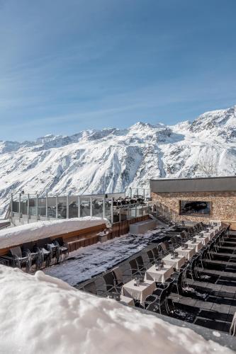 a snow covered building with chairs and tables and mountains at SKI - GOLF - WELLNESS Hotel Riml in Hochgurgl