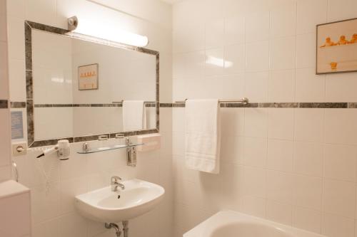 a white bathroom with a sink and a mirror at Jahrhunderthotel Leipzig in Leipzig