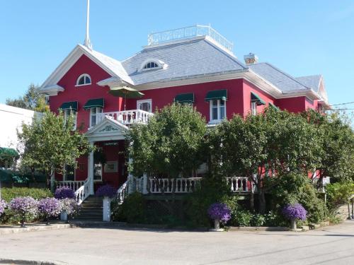 a red house with a white porch and purple flowers at Hôtel-La Grande Maison et Spa in Baie-Saint-Paul