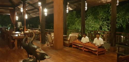 two men sitting on couches in a restaurant with a pelican statue at Hotel Puri Bambu in Jimbaran