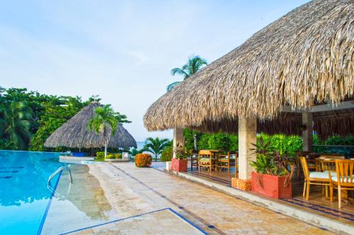 a resort with a swimming pool and thatched umbrellas at GHL Relax Hotel Costa Azul in Santa Marta