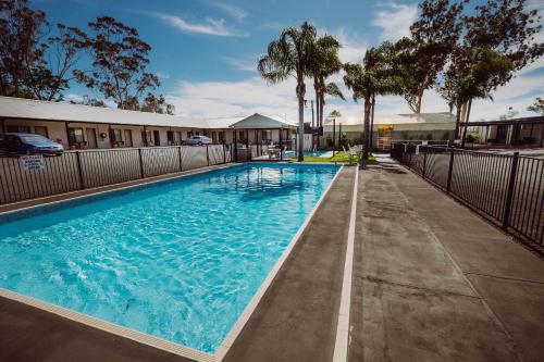 a swimming pool at a hotel with trees and a fence at Artesian Spa Motel in Moree