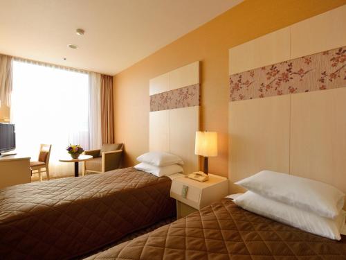 a hotel room with two beds and a desk and a window at Heian No Mori Kyoto in Kyoto